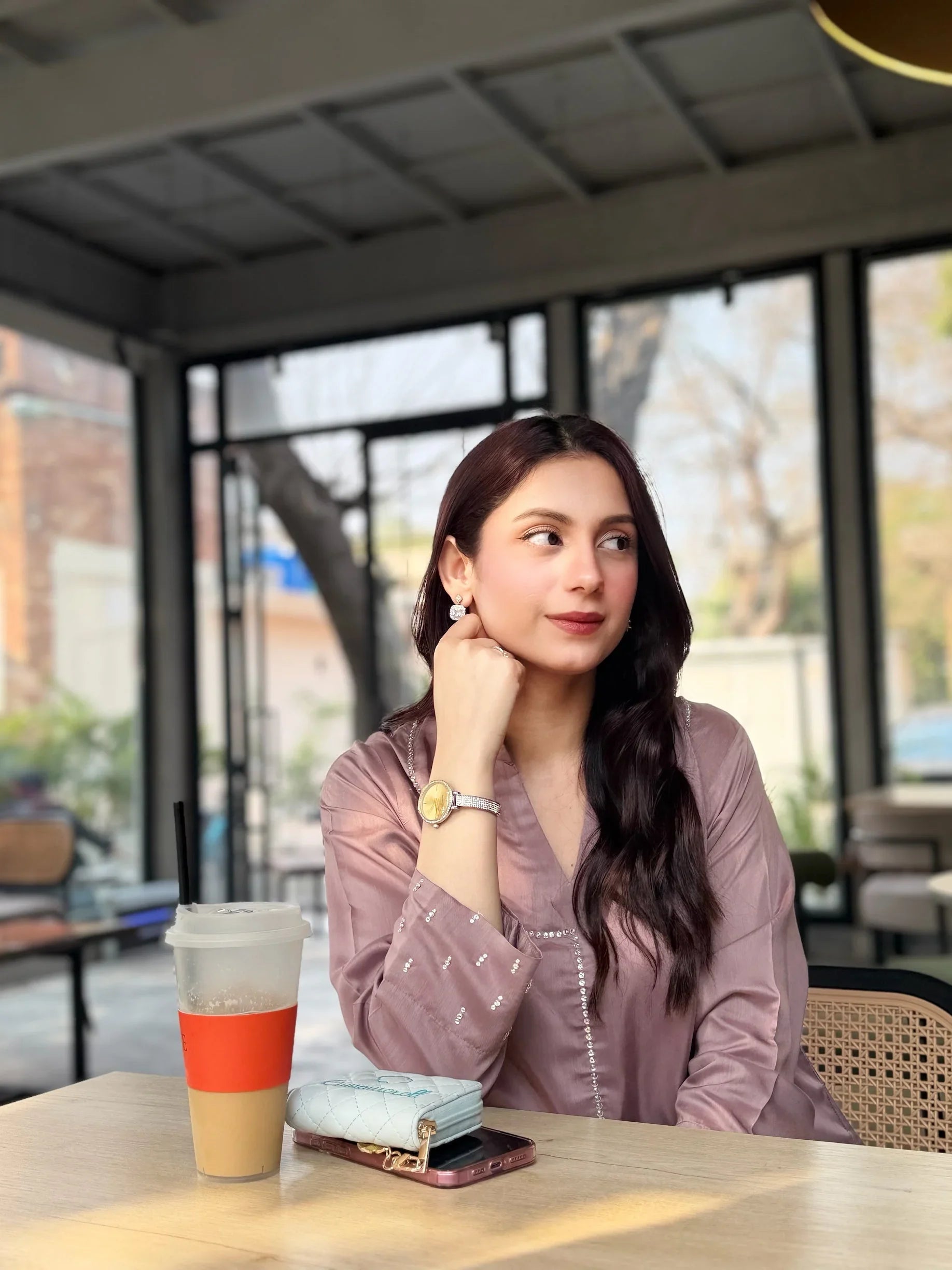 Woman in mauve stitched Pakistani kurta sitting at a cafe table with iced coffee