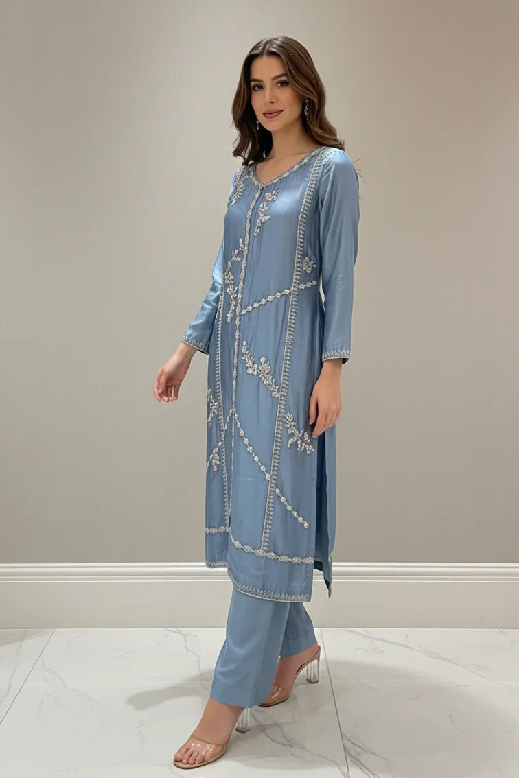 Woman wearing a light blue embroidered outfit against a plain background