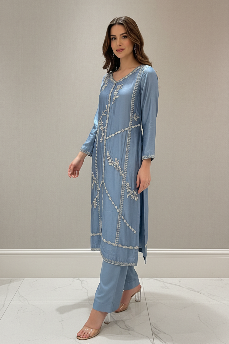 Woman wearing a light blue embroidered outfit against a plain background