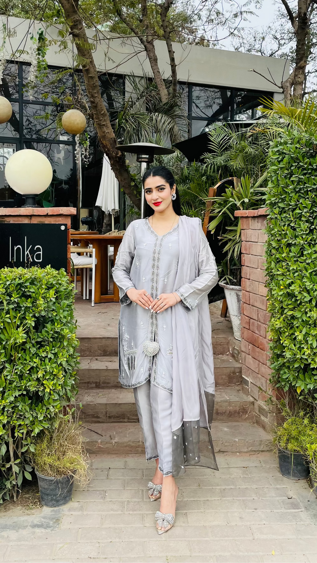 Woman in a gray outfit standing on steps outside a building with greenery.