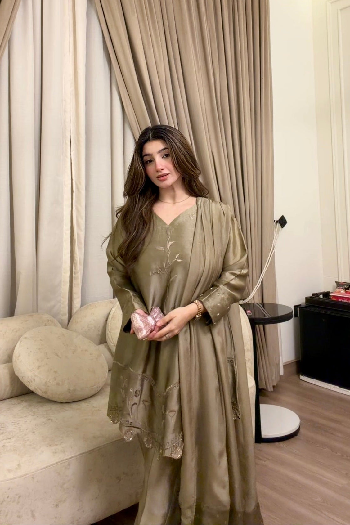 Woman in a green dress standing in a room with beige curtains and a white sofa.